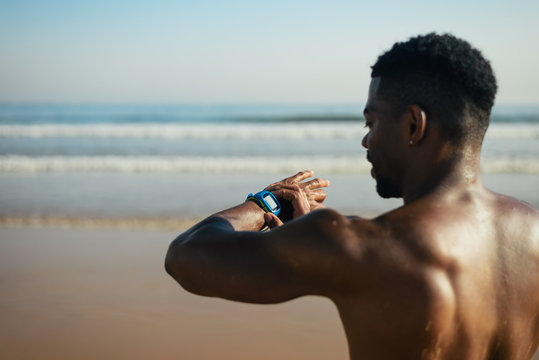 Black athlete timing outdoor beach running or swimming workout on smartwatch. Summer training at the beach.