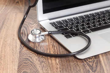 Medical stethoscope with a modern laptop computer on wooden back