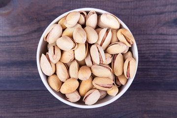 Salted pistachios in a bowl on dark wooden table. Top view with copyspace
