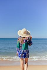 Fototapeta na wymiar Rear view of romantic young lady wearing dress hat on sunny tropical beach background. Summer vacation