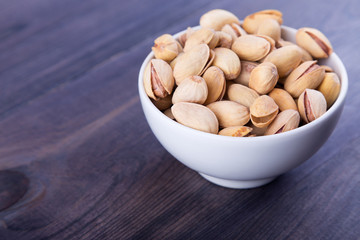 Salted pistachios in a bowl on dark wooden table. Space for text