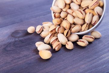 Salted pistachios spill out of the bowl on dark wooden background. Space for text
