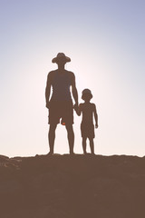 Silhouette of father and son walking in the sunlight, sunny sky background outdoors