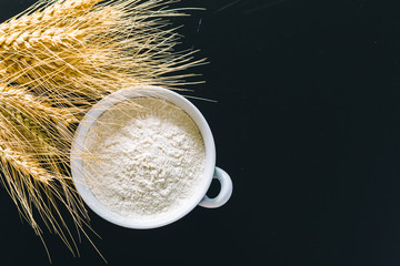 Wheat ears and flour on black background