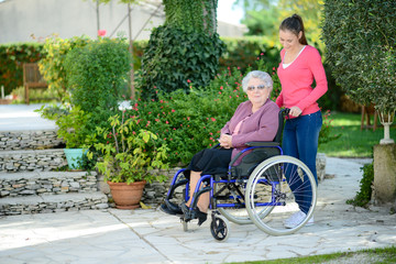 cheerful old woman in wheelchair with her young granddaughter outdoor in hospital