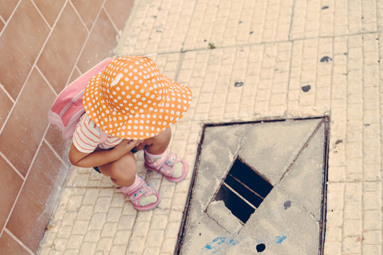 Child looking at hole in pavement, ground outdoors background. Top view