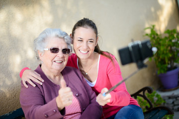 Fototapeta premium cheerful old woman in wheelchair making a selfie with her young granddaughter outdoor in hospital