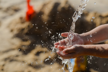 Closeup on child having fun with water on sea beach outdoors background