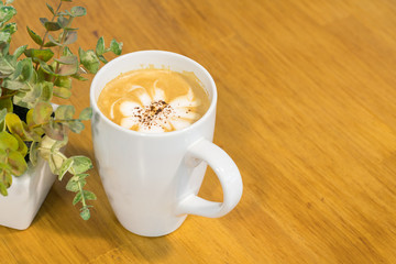 Cup of coffee and small plant in a pot on wooden background
