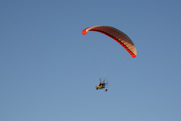 Motorised paraglider flying over mountains in summer day