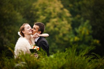 Bride hugs groom's neck while he kisses her cheek