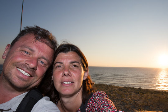 Happy couple taking selfie photo with a smart phone at sunset on the beach