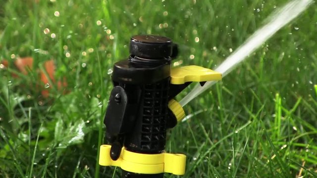 Close Up Slow Motion Water Lawn Sprinkler In Grass / Yellow black watering lawn sprinkler system sprays water on the grass in the garden. Footage is slowed down by half compared with the real time.