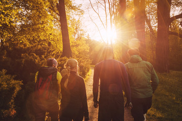 Naklejka na ściany i meble Group of friends walking with backpacks in sunset from back. Adventure, travel, tourism, hike and people friendship concept.