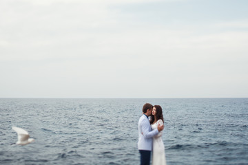 Gulls fly around the wedding couple standing by the blue sea