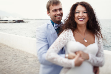 Obraz premium Groom holds bride's waist tightly while they pose by the sea