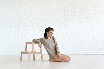 Woman sitting on the wooden chair. Photo in front of white brick wall.