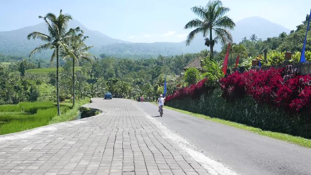 Beautiful views of mountains and palm trees. Cyclist rides in the mountains. Retreat for girls. Beautiful landscape of Bali. Mountain road. Cyclist in red mountains