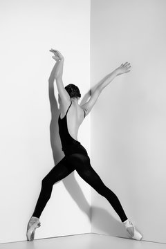 Ballerina in black outfit posing on pointe shoes, studio background.