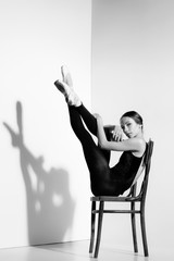 Ballerina in black outfit posing on a wooden chair, studio background.