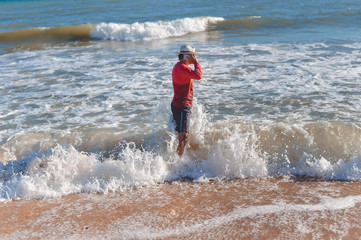 Handsome active man using smartphone, seaside background. Back side view
