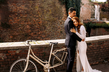 Man in black suit hugs delicate woman standing before the bicycl