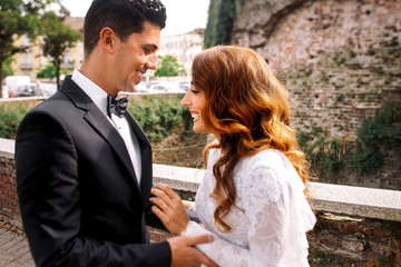 Laughing bride with red hair stands before a groom on the street