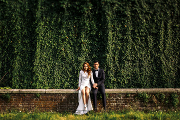 Groom and bride with naked legs sit on the brick wall
