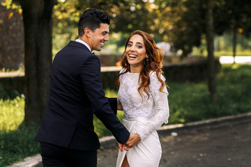Italian bride with broad smile holds groom's hand while walking