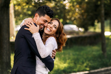 Bride and groom hug each other tightly while laughing in the par