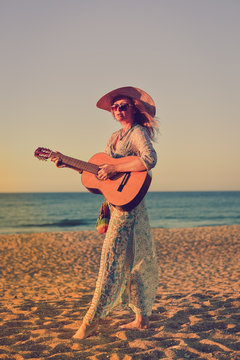 Romantic beautiful female musician at the beach with guitar, outdoors background