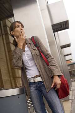 femme qui fume devant un cendrier dans une ville