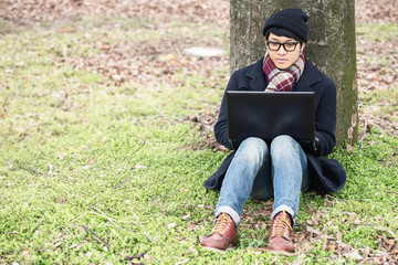Obraz premium Man sitting under a tree by a computer.