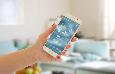 Smart home control of temperature, safety and environment in home. Mobile app on display. Living room in background. © Stanisic Vladimir