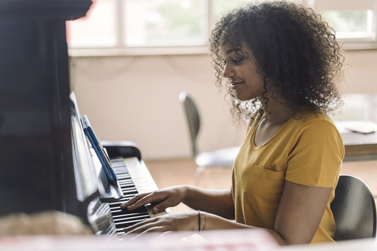 Young woman playing piano, reading notes from digital tablet