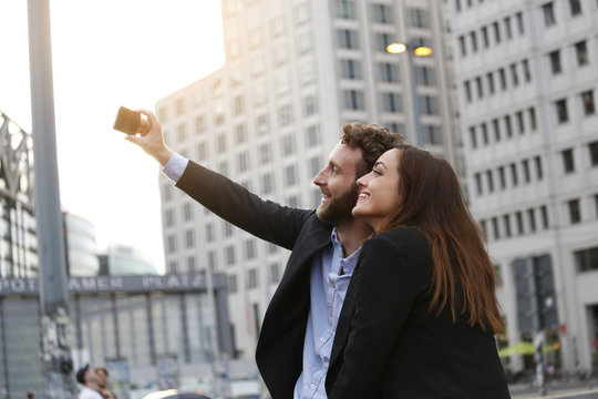 Smiling young businessman and businesswoman taking selfie outdoors