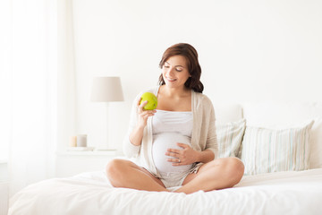 Obraz na płótnie Canvas happy pregnant woman eating green apple at home