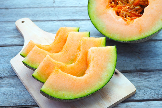 Close up of sliced rock melon on a wooden cutting board.