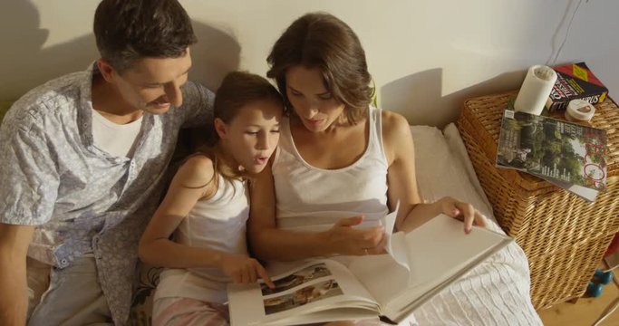Mother, father and daughter wearing pajamas reading a book together laying in bed