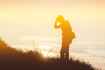 silhouette  woman with a camera bag on a meadow at sunset