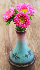 Pink daisies in fine porcelain vase on wooden surface
