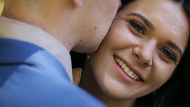 Close-up beautiful brunette bride smiling while groom whispering compliments to her