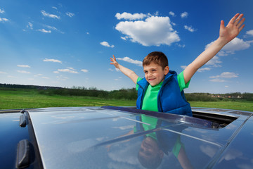 Smiling kid boy enjoying freedom on sunroof of car