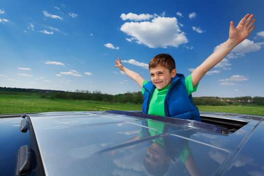 Smiling kid boy enjoying freedom on sunroof of car