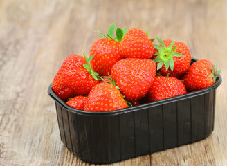 Fresh strawberries in plastic box on wooden surface
