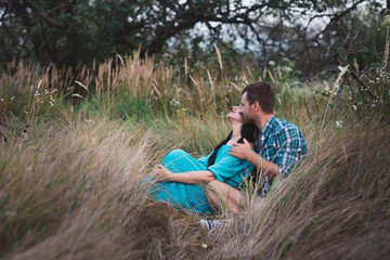 Naklejka na ściany i meble Shot of young man and woman sitting together outdoors on grass field. Romantic young couple in meadow,love,relatonships,lifestyle
