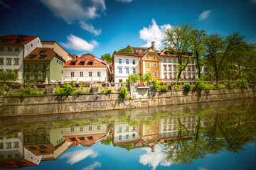 Fototapeta na wymiar View on Ljubljanica river with old building in Ljubljana city in Slovenia. Long exposure image technic with blurred clouds and reflection on the water