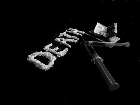 Cocaine drug powder in shaped death word, two crossed injections, credit card and hundred euro banknote on black background in black and white colors
