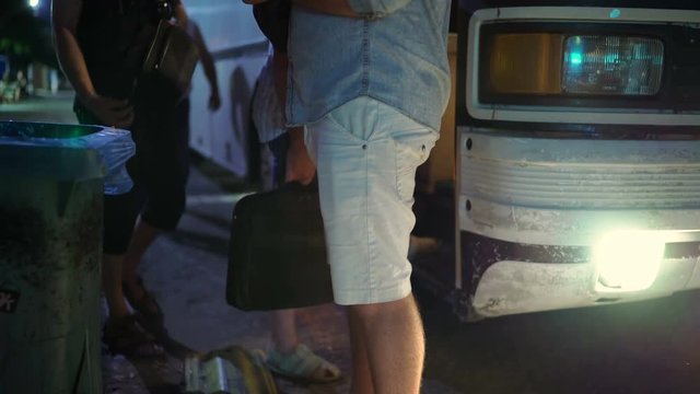 Passengers boarding long distance intercity coach at night bus stop closeup shallow focus