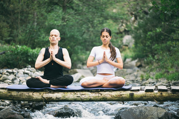 Beautiful young woman meditating in yoga pose at a mountain stream with her teacher. 